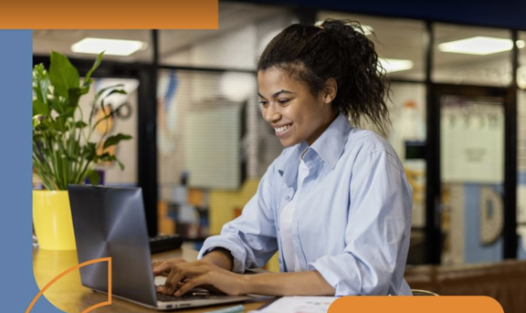 A young woman smiles and types at a laptop
