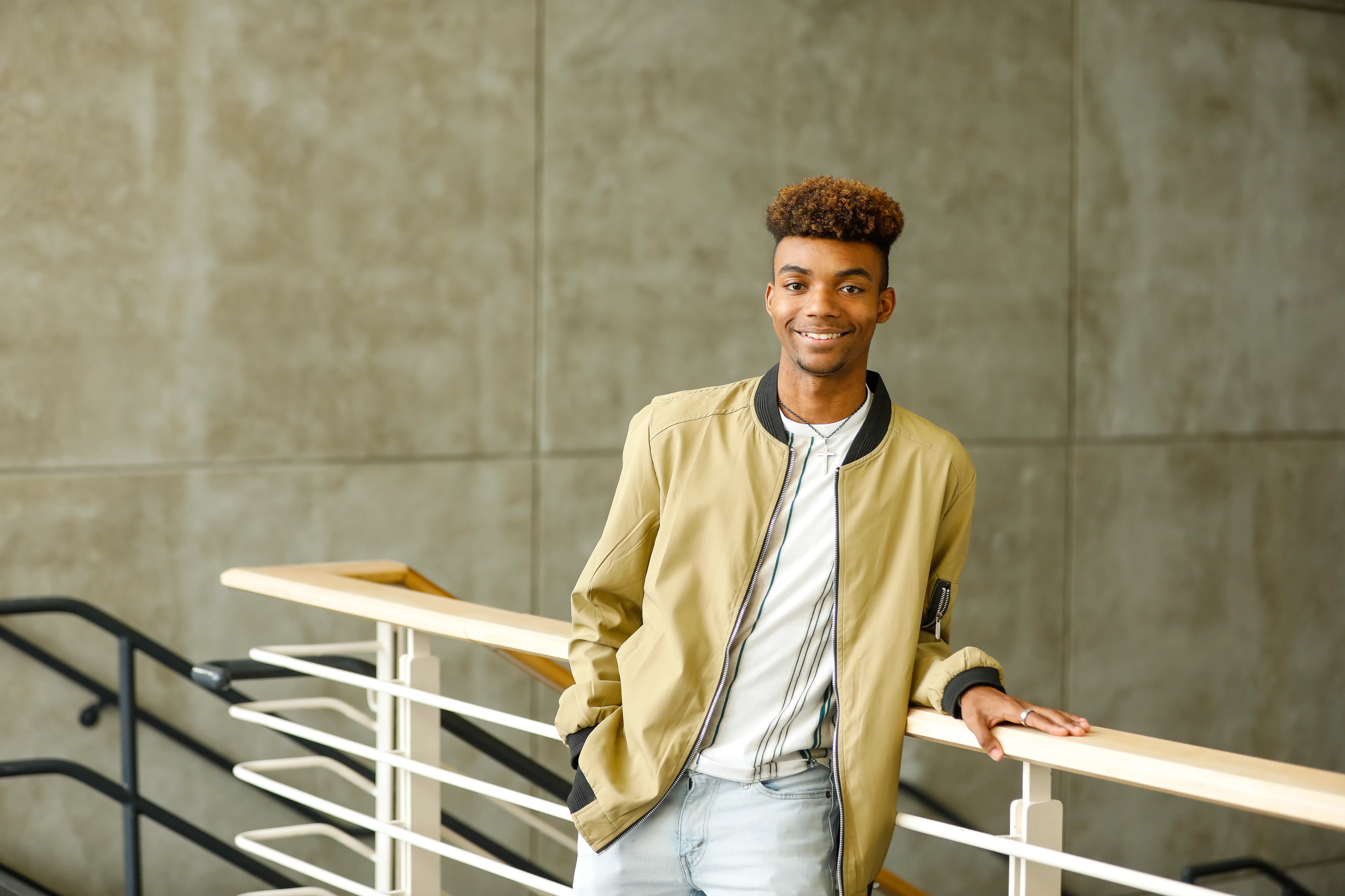 A young man leans against a railing and smiles