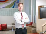 A business man wearing a white dress shirt, red plaid tie, and black trousers stands confidently with his arms crossed